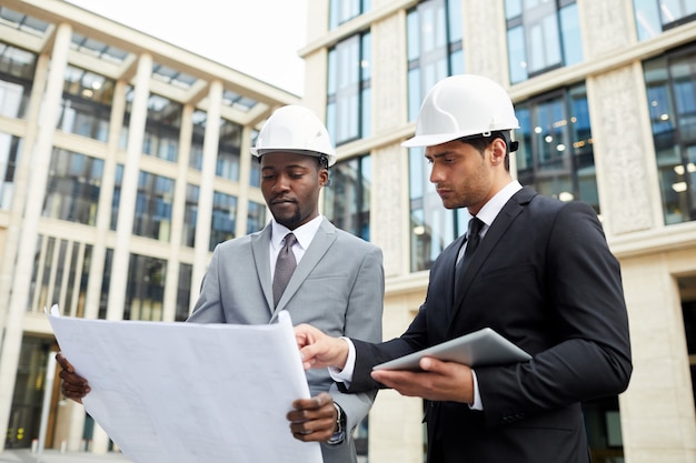 Captura de la cintura de dos arquitectos con cascos que trabajan con planos de pie al aire libre