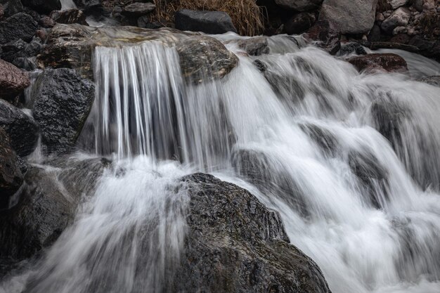 Captura de um riacho de montanha com uma cachoeira corre sobre as pedras entre as margens rochosas