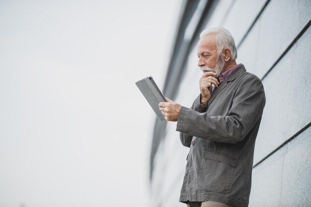 Captura de un exitoso hombre de negocios senior que usa una tableta digital frente a un edificio corporativo.