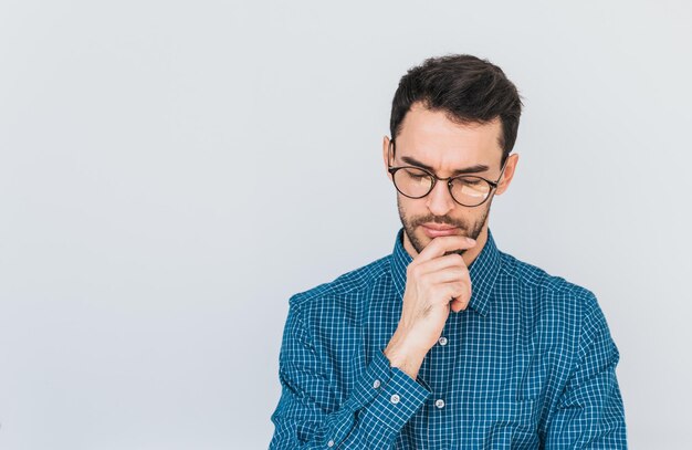 Captura de pantalla de un apuesto y serio modelo masculino pensativo con gafas y camisa azul mirando hacia abajo pensando en el problema de sostener su barbilla Concepto de personas y negocios Copiar espacio para su anuncio