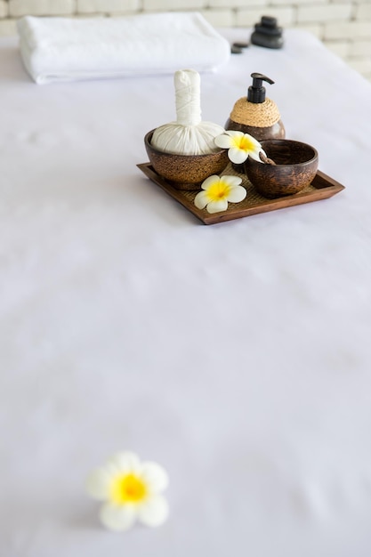 Captura de pantalla de masajes tailandeses, bolas de compresas de toallas herbales, aceite de coco, perfumes, cosméticos y flores de plumeria en una bandeja de madera colocada en una cama de masaje en terapia de spa preparándose para el cliente.