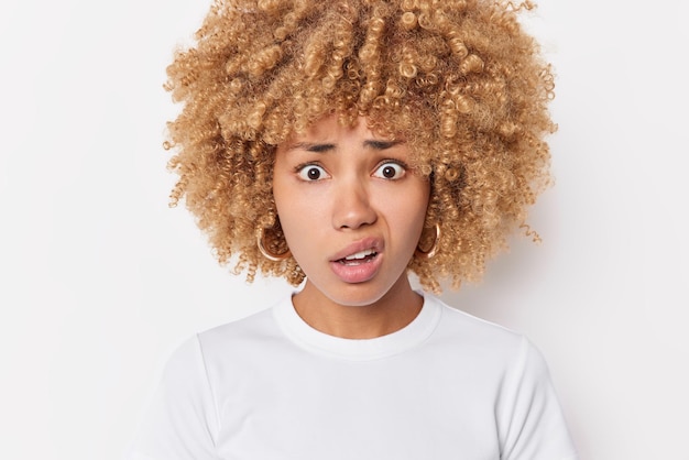 Captura de pantalla de una mujer europea de cabello rizado disgustada que frunce los labios con expresión preocupada que usa ropa informal posa contra un fondo blanco y escucha algo desagradable. Concepto de reacciones humanas