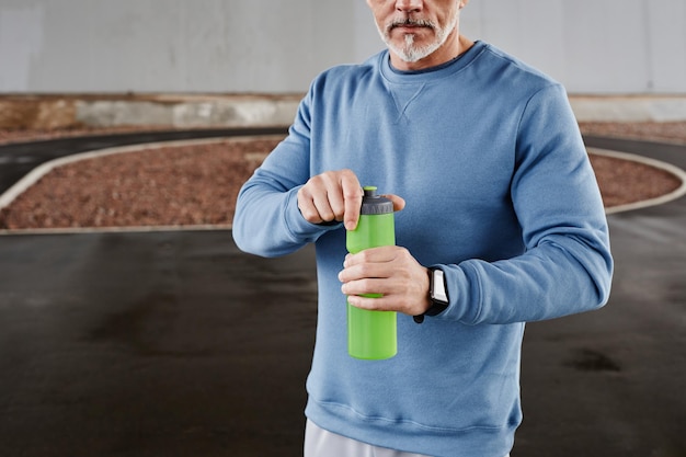 Captura recortada de un anciano irreconocible sosteniendo una botella de agua durante el entrenamiento al aire libre en setti urbano