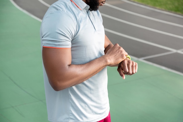 Foto captura recortada de un atleta afroamericano de pie en el estadio mientras mira su rastreador de fitbit