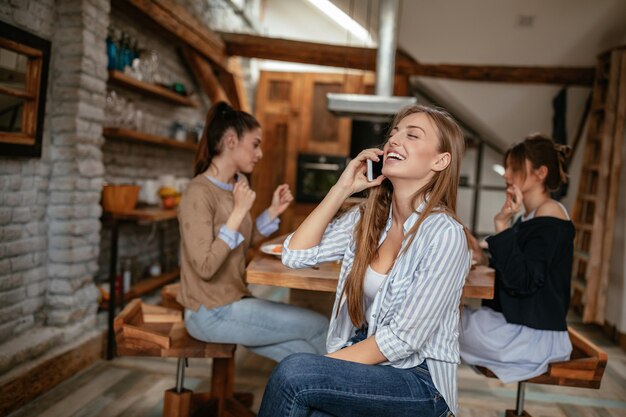 Captura recortada de una atractiva joven rubia que tiene una llamada telefónica mientras desayuna con amigos