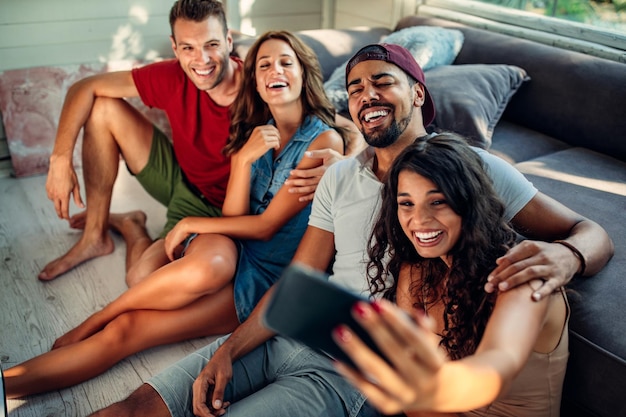 Captura recortada de cuatro amigos felices tomándose una selfie en la sala de estar