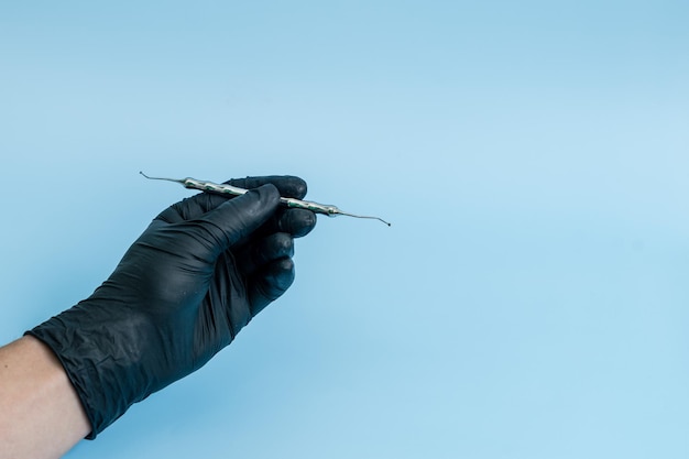 Captura recortada de dentista profesional en guantes médicos negros con herramienta dental Concepto dental aislado sobre fondo azul