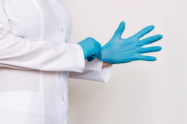 Captura recortada de una doctora con una bata blanca que se pone guantes médicos azules antes de examinar al paciente