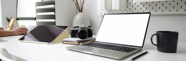 Captura recortada del escritorio de oficina con pantalla en blanco portátil, suministros de oficina y taza de café