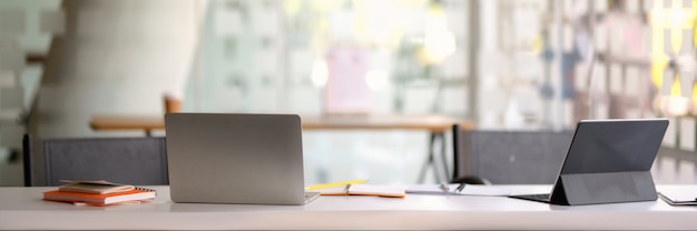 Captura recortada del espacio de trabajo portátil con computadora portátil y tableta en la oficina de pared de vidrio