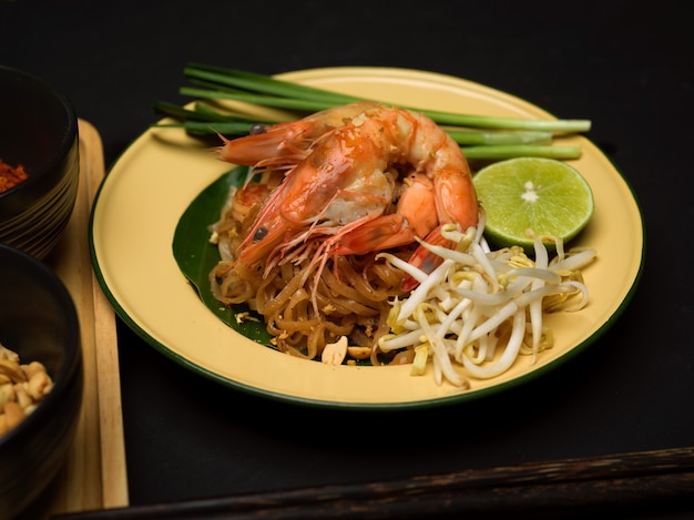 Captura recortada de fideos tailandeses revueltos con camarones que sirven en un plato tradicional con limón, brotes de soja y cebollino, Pad Thai