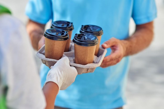 Captura recortada de un hombre que recibe cuatro tazas de café de un mensajero masculino con guantes protectores