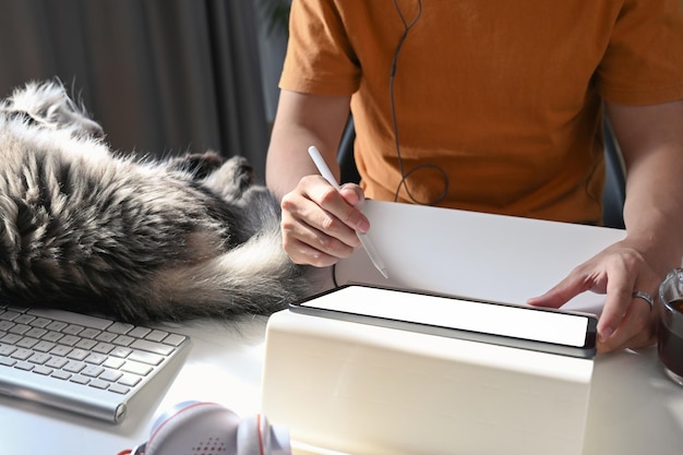 Captura recortada del hombre que usa la tableta digital y su gato durmiendo en el escritorio blanco