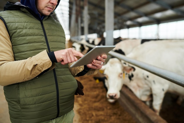 Foto captura recortada de un joven agricultor o propietario de una granja de vacas apuntando a la pantalla de la tableta