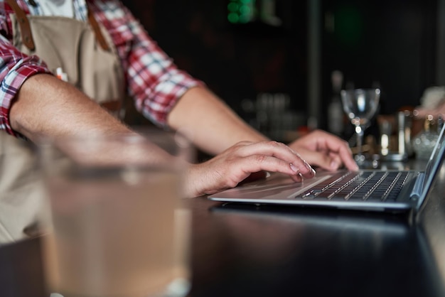 Foto captura recortada de un joven barista tomando notas y usando una computadora portátil