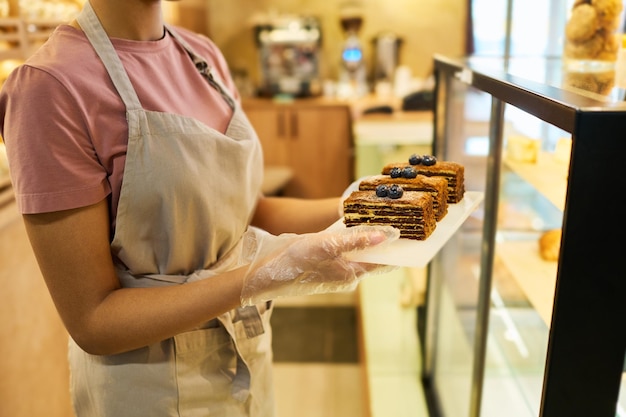 Captura recortada de un joven empleado en un delantal sosteniendo una tabla con tres pasteles