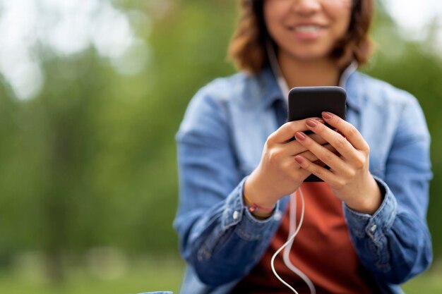 Captura recortada de una joven mujer sonriente en auriculares usando un teléfono inteligente al aire libre