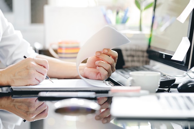 Captura recortada de la mano del hombre usando la escritura a lápiz en el portapapeles mientras está sentado en el escritorio de la oficina y trabajando con la computadora.