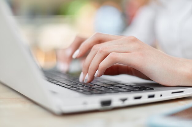 Captura recortada de manos femeninas con bonitos teclados de manicura en la computadora portátil, funciona desde casa, se sienta a la mesa y busca en internet