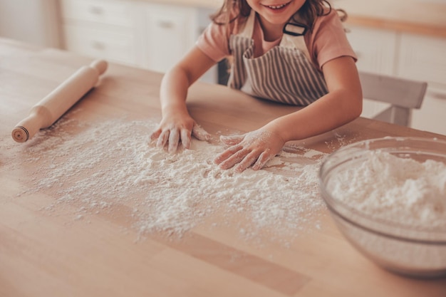 Captura recortada de manos de niña jugando con harina en la mesa de la cocina