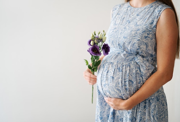 Captura recortada de mujer embarazada irreconocible sosteniendo flores tocando acariciando barriga sobre fondo blanco Hermoso embarazo feliz saludable en primavera verano concepto de alergia Copyspace