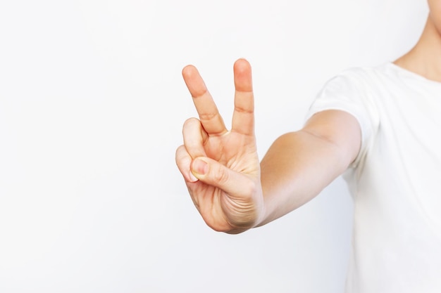 Captura recortada de una mujer joven con una camiseta blanca que muestra un gesto de paz Signo de la mano de la victoria