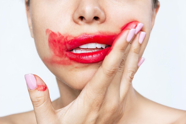 Captura recortada de una mujer joven untando lápiz labial de color rojo brillante en la cara con la mano