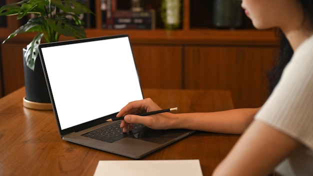 Captura recortada de una mujer que usa una computadora portátil en un escritorio de madera que trabaja en línea en la oficina en casa