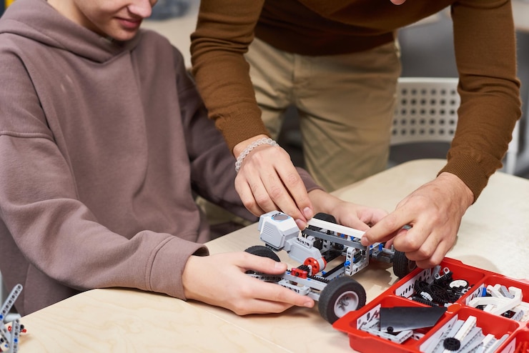 Foto captura recortada de un niño irreconocible que construye un automóvil eléctrico en clase de robótica e ingeniería en la escuela, espacio de copia