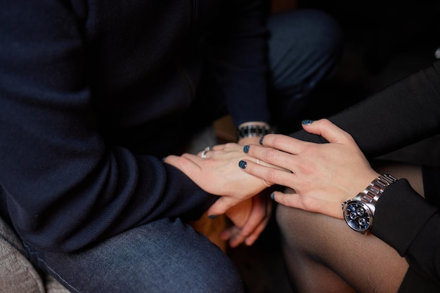 Captura recortada de una pareja joven tomándose de la mano mientras se sientan juntos. Centrarse en las manos.