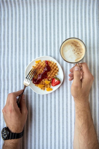 Captura recortada de una persona comiendo gofres caseros recién hechos y bebiendo café en el desayuno