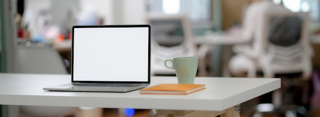 Captura recortada de simple escritorio de oficina con pantalla en blanco portátil, taza y cuaderno