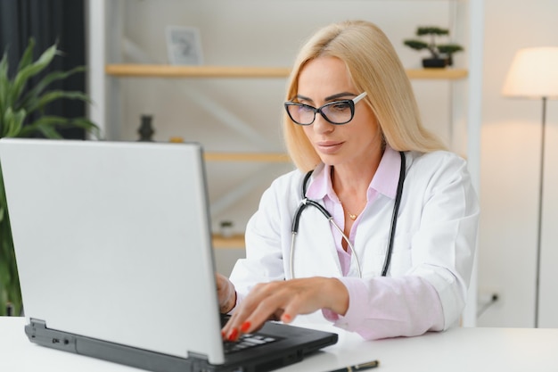 Captura de retrato de una doctora de mediana edad sentada en el escritorio y trabajando en el consultorio médico