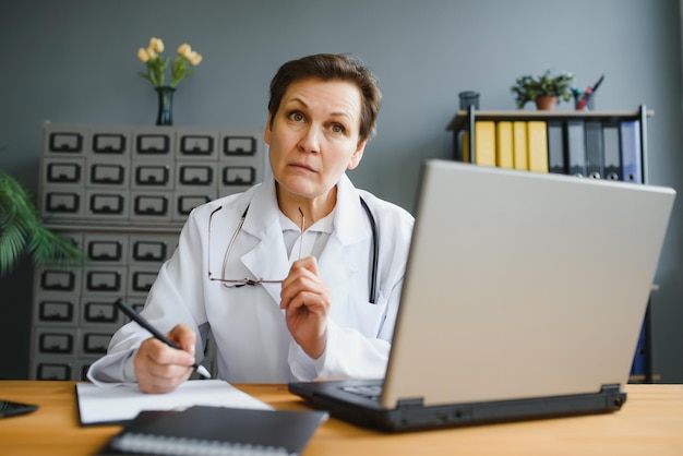 Captura de retrato de una doctora de mediana edad sentada en el escritorio y trabajando en la oficina