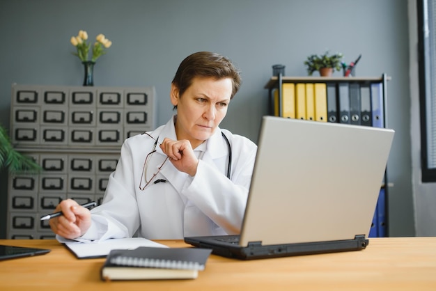 Captura de retrato de una doctora de mediana edad sentada en el escritorio y trabajando en la oficina