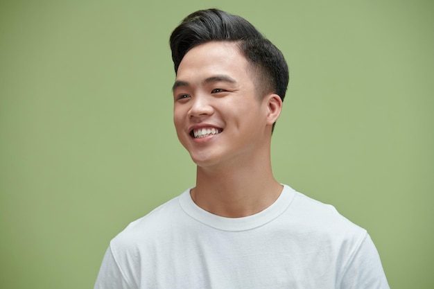 Captura de retrato de un joven asiático adulto sonriendo posando sobre fondo de pared verde