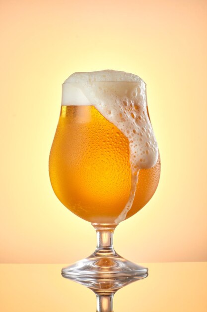Foto captura vertical de cerveja em um copo com gotas de água sobre um fundo amarelo