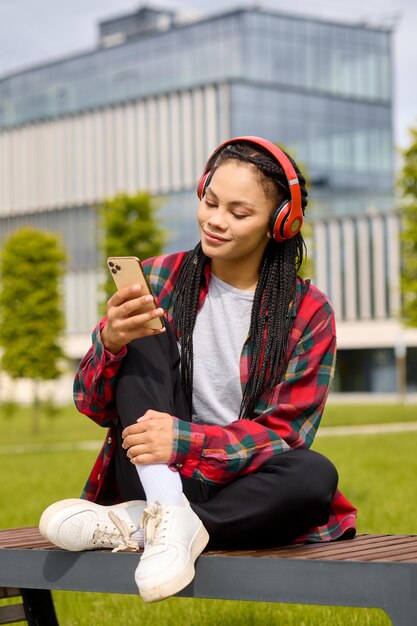 Capturada en un momento sereno, una mujer afroamericana se sienta pensativamente en un banco mientras escucha las melodías de su lista de reproducción cuidadosamente seleccionada.