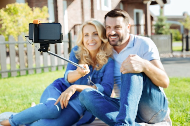 Capturando momentos. La atención se centra en un palo sefie en las manos de una hermosa mujer sentada uniéndose a su amado esposo mientras se toman una selfie juntos