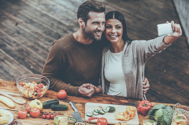 Capturando momentos brilhantes juntos. vista superior de um lindo casal jovem fazendo selfie e sorrindo enquanto preparam a comida juntos