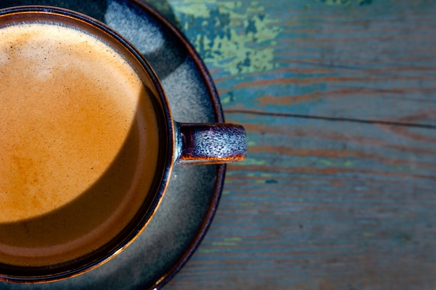 Foto capuchino con espuma, taza de café azul sobre fondo de madera