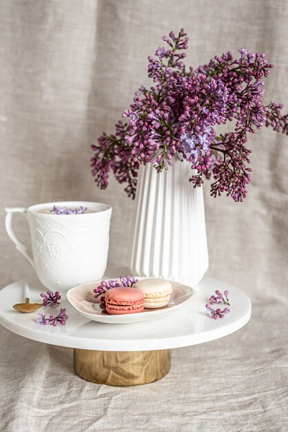 Capuchino con macarrones sobre mantel de lino, flores lilas violetas, concepto de mañana