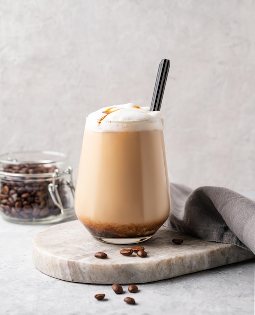 Capuchino o café con leche con espuma de leche y caramelo en un vaso con granos de café sobre fondo de mármol claro Vista frontal y espacio para copiar
