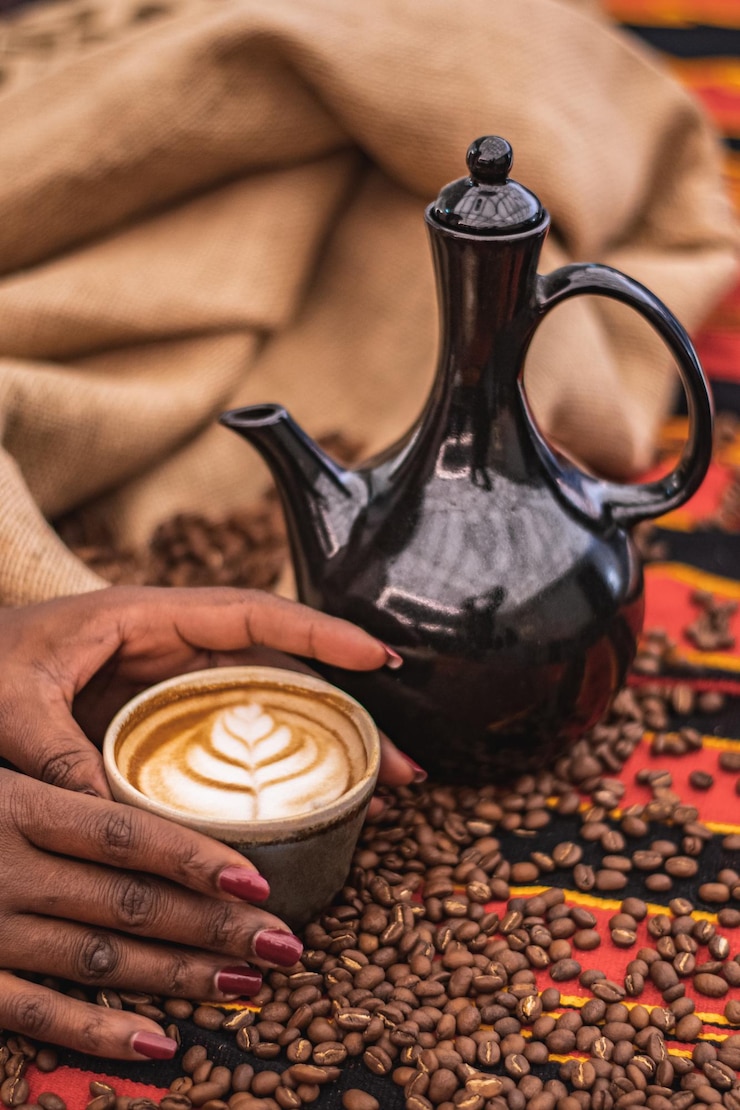 Foto capuchino en una taza de cerámica con flores o hojas dibujadas en la tetera de espuma y granos de café tostados