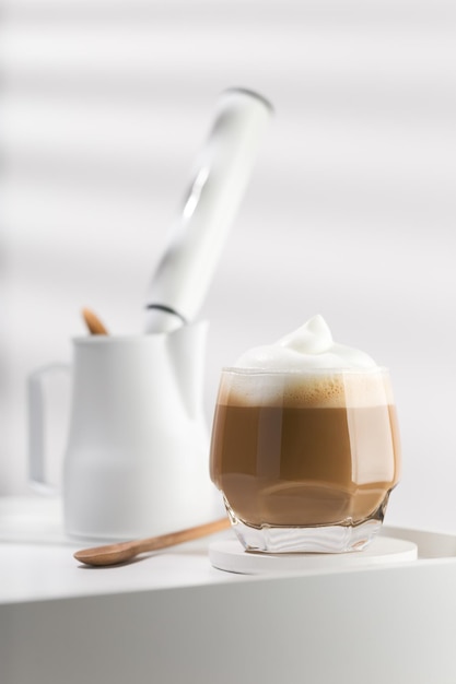 Capuchino en un vaso de vidrio sobre una mesa de madera blanca Café y espuma de leche