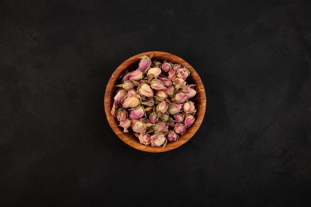 Capullos de rosa rosa secos en un cuenco de madera sobre una vista superior de fondo con textura oscura