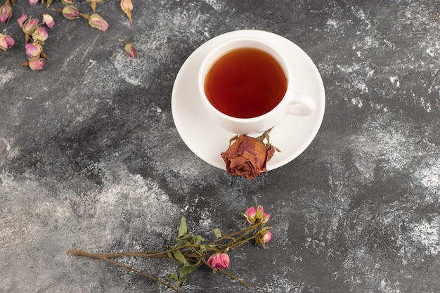 Capullos de rosa secos con una taza de té caliente colocados sobre una mesa de piedra.