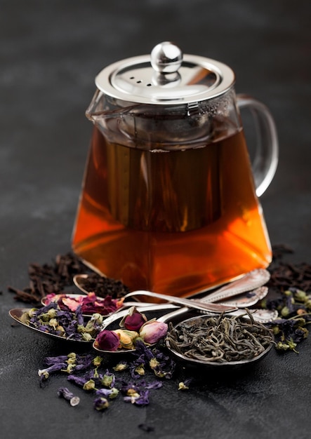 Capullos de rosaflores de malva azulté verde y negro suelto con azúcar y tetera de vidrio con cucharas