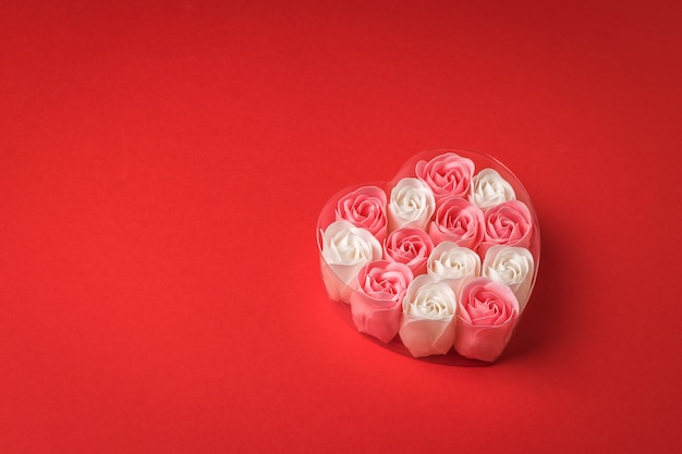 Capullos de rosas rojas y blancas en una caja en forma de corazón sobre un fondo rojo. El concepto de amor.