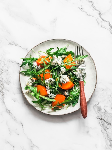 Caqui rúcula gorgonzola salada vegetariano lanche sazonal aperitivo em uma vista superior de fundo claro